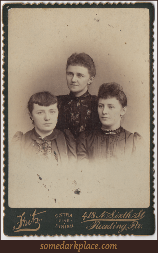 Three young women all in formal dresses. Two have hair curled in the front, one has bangs, all have their hair pulled back. All have their ears pierced and wear pendant or loop earrings. Various other pieces of jewelry are in the photo.