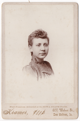 A headshot of an attractive young woman perhaps in her late teens. She is wearing a dress with a high collar and elaborate decorative piping. Her hair is curly in the front and pulled back or short.