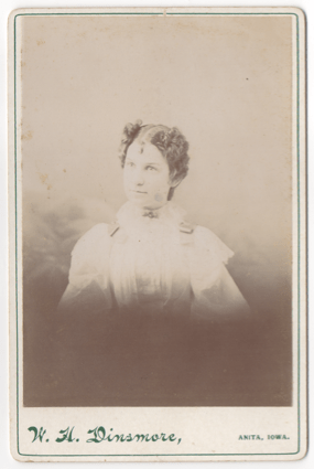 A young woman with a severe part down the middle of her head. She is wearing all white. She has decorative buckles or ribbons on her shoulders and a broach at her throat.
