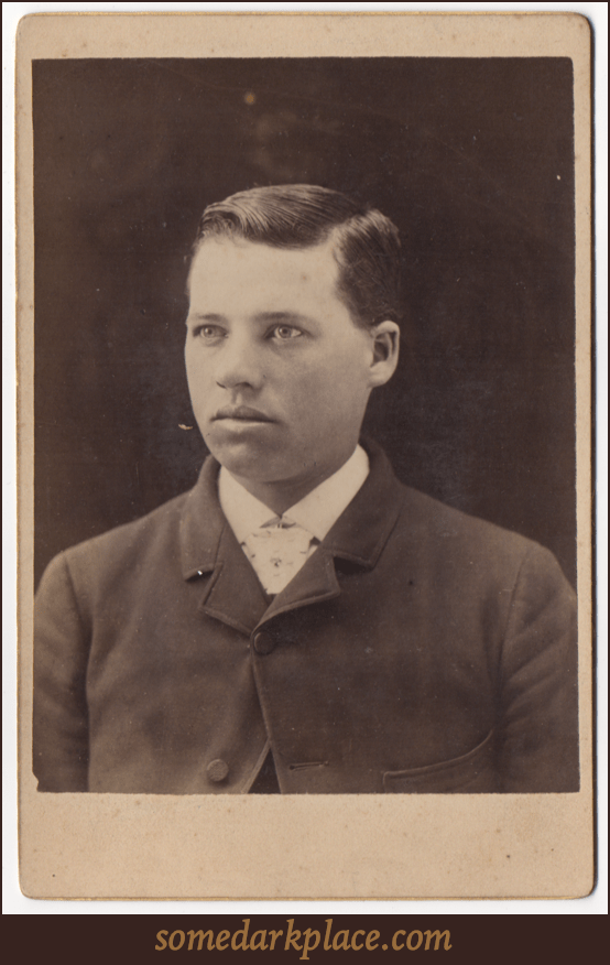 A handsome young man. He's wearing a suit coat and a white collared shirt. He appears to be wearing a tie of some sort. His hair is parted on the left.