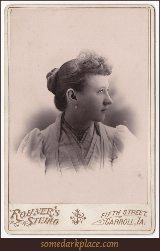 A profile of an attractive young woman looking over her left shoulder. She has a drop earring with a bright stone hanging from her right earlobe. Her dress is white and layered. The lighting is dramatic.