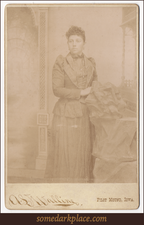 A young woman in a full length dress. This is an obvious studio shot with a prop rock and a painted background.
