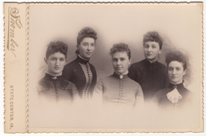 Five young and attractive women. Four of the five are wearing high collars and elaborate dresses with the fifth in simpler garb.